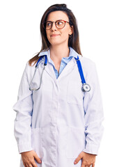 Fototapeta premium Young beautiful woman wearing doctor stethoscope and glasses smiling looking to the side and staring away thinking.