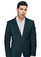 Handsome hispanic man wearing business clothes in shock face, looking skeptical and sarcastic, surprised with open mouth