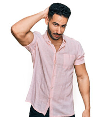 Hispanic man with beard wearing casual shirt confuse and wonder about question. uncertain with doubt, thinking with hand on head. pensive concept.