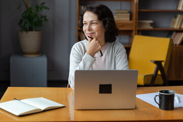 Confident stylish european middle aged senior woman using laptop at home. Stylish older mature 60s...