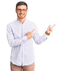 Handsome young man with bear wearing elegant business shirt and glasses smiling and looking at the camera pointing with two hands and fingers to the side.