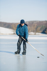 An elderly man practices ice hockey on a frozen lake in winter.