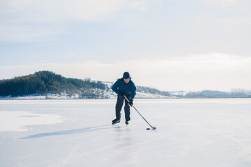 Fototapeta na wymiar An elderly man practices stricking the puck with hockey sticks on a frozen lake in winter.