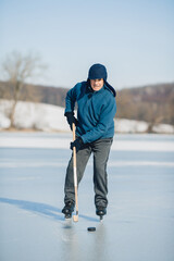 Fototapeta na wymiar An elderly man practices ice hockey on a frozen lake in winter.