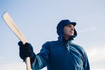 Portrait of an elderly man with a hockey stick against the background of the sky.