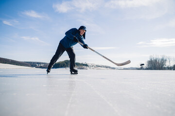 An elderly man practices stricking the puck with hockey stick on a frozen lake in winter.