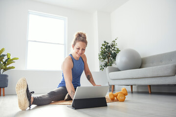 Cheerful active woman doing fitness at home, using tablet, watching online lessons.