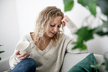 Exhausted frustrated young woman touching forehead, sitting on couch alone.