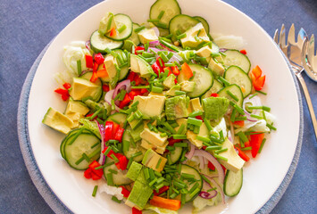 fresh green salad with cucumber, avocado, onions and lettuce on white plate