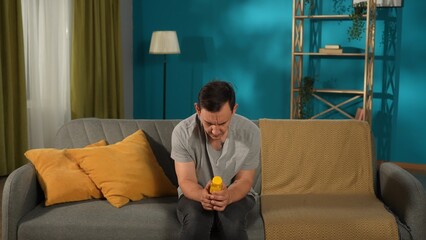 A mentally unstable man sits on a sofa with a bottle of pills. Concept for depression, suicide,...