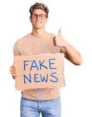 Young handsome man holding fake news banner smiling happy and positive, thumb up doing excellent...