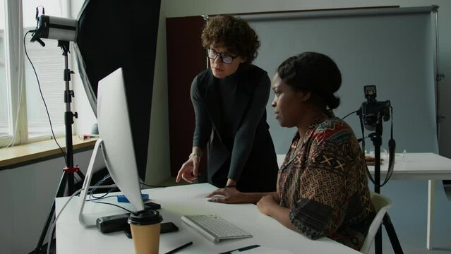 Professional female stylist and photographer discussing reference image on computer before commercial shoot in studio