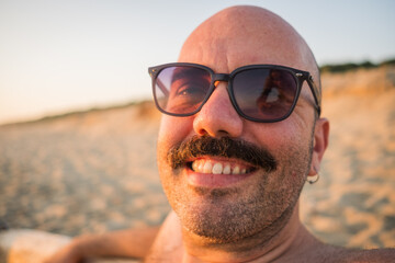 close up portrait of caucasian male wearing sunglasses with moustache sit on the beach summer...