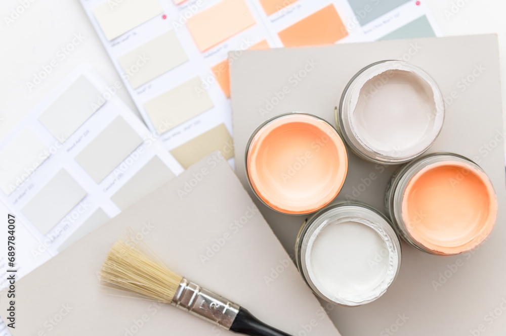 Wall mural Tiny sample paint cans during house renovation, process of choosing paint for the walls, Peach Fuzz color of the year 2024, color charts on background