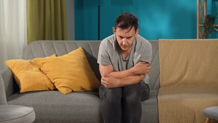 A mentally unstable man is sitting on a sofa in the living room close up. Concept for depression,...
