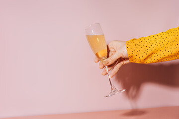 Lady hand with gold-painted nails holding a glass of champagne against a pink background.
