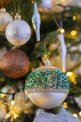 Festive glass balls with colored sparkles, Christmas tree and yellow bokeh of glowing garland.