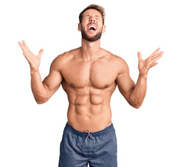 Young caucasian man standing shirtless celebrating mad and crazy for success with arms raised and...