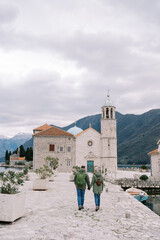 Couple walk holding hands towards the Church of Our Lady of the Rocks. Back view. Montenegro