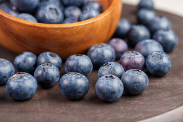 A pile of fresh blue bilberry on a brown board with wooden bowl. Ripe blueberries.