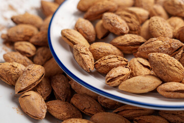 White ceramic dish with delicacy roasted almond nuts in cracked nutshell.