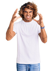Young hispanic man wearing casual white tshirt shouting frustrated with rage, hands trying to strangle, yelling mad