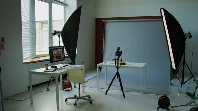 Interior of photo studio with no people. There is desk with computer, light setup, camera on tripod, cyc wall and table with food arranged for shoot