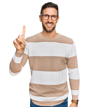 Handsome man with beard wearing casual clothes and glasses pointing finger up with successful idea. exited and happy. number one.