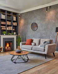 Barrel chair and round coffee table near gray corner fabric sofa against the wall with fireplace and bookshelves design. The interior design of the modern living room