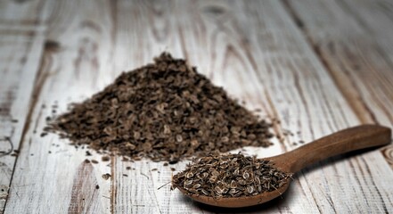 Natural wooden background with a spoon and a pile of dried dill seeds. Plant, food and medical themes. The concept of the usefulness of dill.