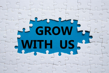 Grow with us symbol. Concept words Grow with us on white puzzle. Beautiful blue background. Business and Grow with us concept. Copy space.