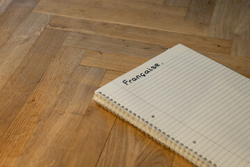 Fototapeta premium Blank notepad in class on wooden desk for student learning French written language. Française subject for adult learning with handwritten notes and writing exercises for personal development