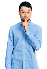 Hispanic man with beard wearing casual business shirt asking to be quiet with finger on lips....