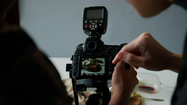 Close up shot of hands of female photographer and food stylist discussing image on viewfinder of professional digital camera while taking food photos in studio