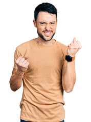Hispanic man with beard wearing casual t shirt celebrating surprised and amazed for success with arms raised and eyes closed. winner concept.