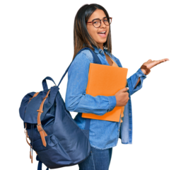 Young latin girl wearing student backpack and holding books pointing aside with hands open palms showing copy space, presenting advertisement smiling excited happy
