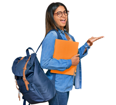 Young latin girl wearing student backpack and holding books pointing aside with hands open palms showing copy space, presenting advertisement smiling excited happy