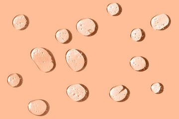 Cosmetic hydrating product or ingredient concept. Peach fuzz color drops of transparent liquid on a trendy color background. Drops gel or oil close up.