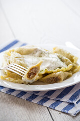 cooked dumplings with meat, spices and sour cream, in a plate on a light wooden table.
