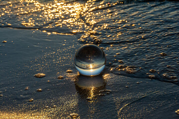 Glass ball lies in the water in the waves at the sea