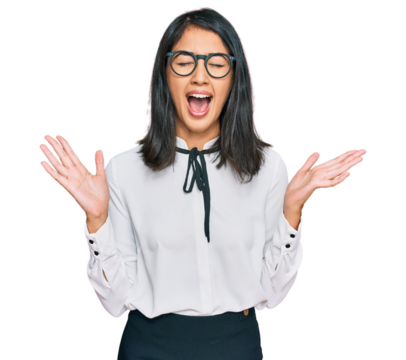 Beautiful asian young woman wearing business shirt and glasses celebrating mad and crazy for success with arms raised and closed eyes screaming excited. winner concept