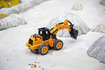 A yellow plastic children's excavator against a background of white piles of hills. Toys...