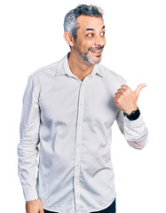 Fototapeta premium Middle age hispanic with grey hair wearing casual white shirt smiling with happy face looking and pointing to the side with thumb up.