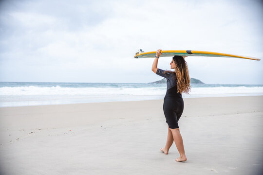 Mulher jovem na praia segurando sua prancha se surf acima de sua cabeca.