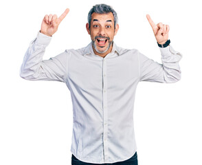 Naklejka premium Middle age hispanic with grey hair wearing casual white shirt smiling amazed and surprised and pointing up with fingers and raised arms.