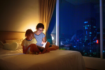 Child and mother read a book in dark room.