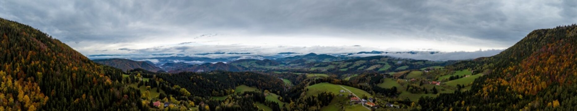 Aerial panoramic view of the mountains and the surrounding forests in fall near Graz under a cloudy sky, Semriah, Styria, Austria.