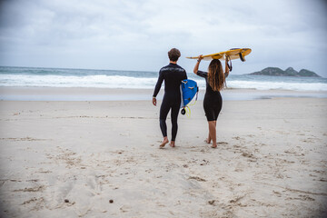 Couple of surfers walking along the beach with their boards above their heads. Rear view.