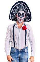 Man wearing day of the dead costume over background in shock face, looking skeptical and sarcastic, surprised with open mouth