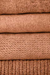 Fototapeta na wymiar stack of warm knit sweaters on white table and gray background. Cold autumn season texture detail peach color of the year 2024
